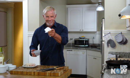 A man in the kitchen holding something up to his mouth.