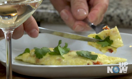 A person cutting into an omelet with cilantro.